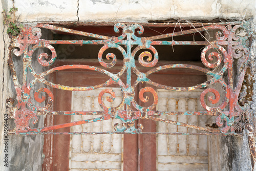 Rusty painted old ornate decorative wrought iron grill in front of door photo