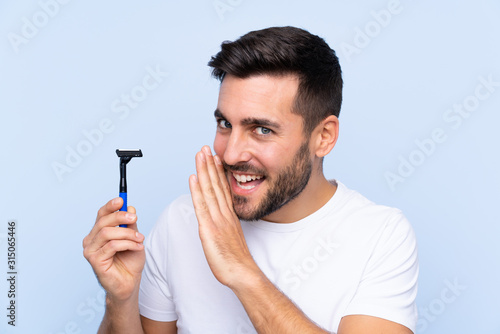 Young handsome man shaving his beard over isolated background whispering something