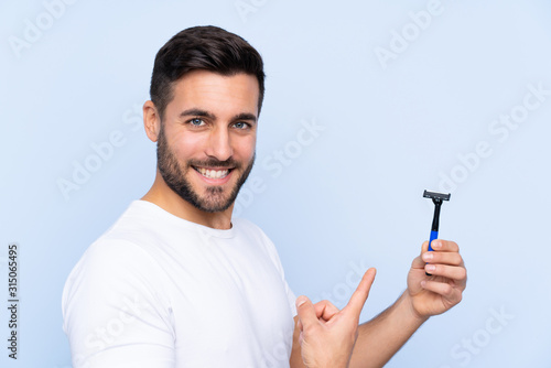 Young handsome man shaving his beard over isolated background and pointing it