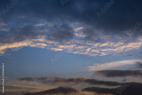 blurred dark sky background with evening fluffy curly rolling clouds with setting sun. Good windy weather