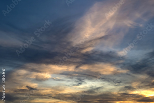 blurred dark sky background with evening fluffy curly rolling clouds with setting sun. Good windy weather