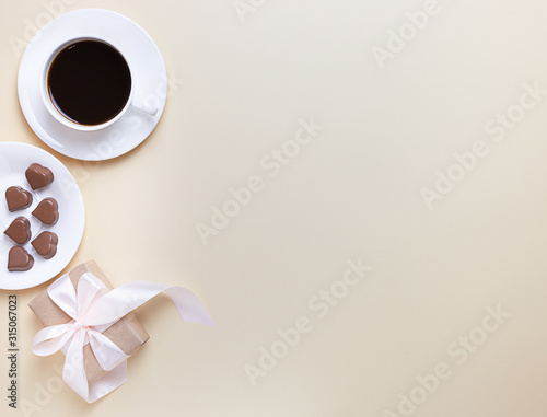 Banner of Valentine's Day. A Cup of coffee, a gift box and a heart-shaped chocolate on a neutral beige background.