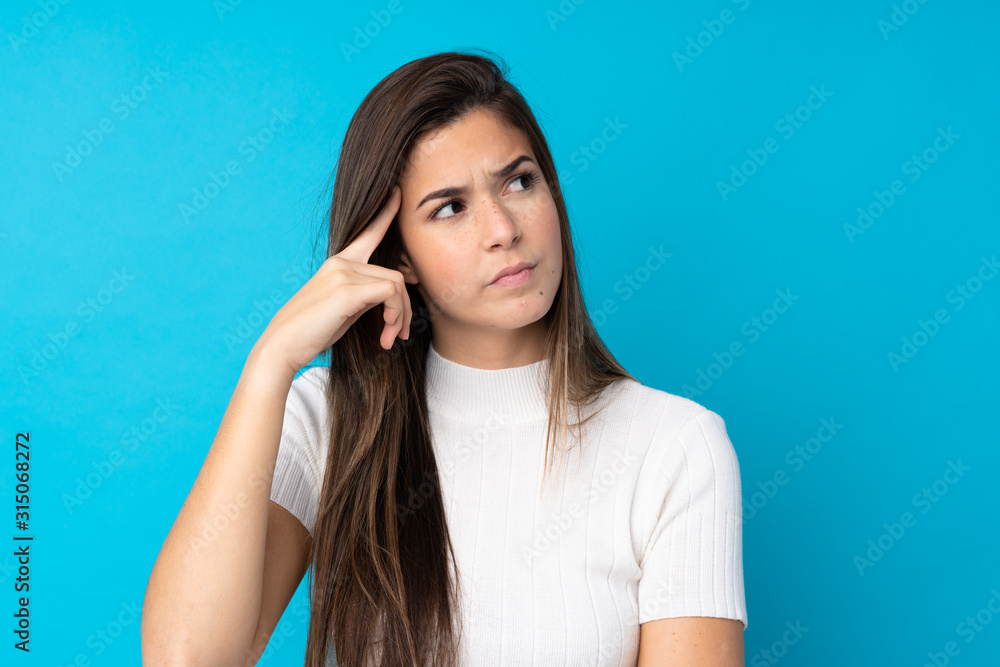 Fototapeta premium Teenager girl over isolated blue background making the gesture of madness putting finger on the head