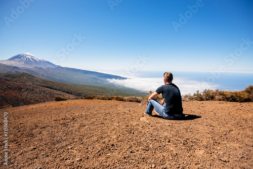 A young male traveler sits on the sand and looks at the top of the Teide volcano. Teide National Park, Canary, Spain