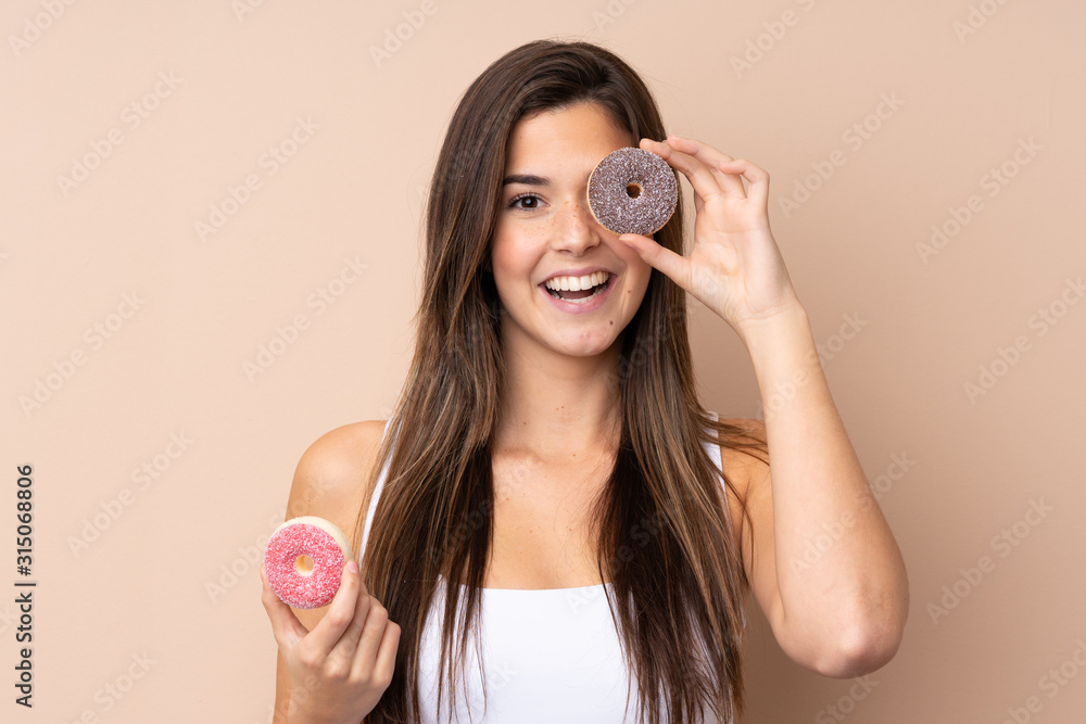 Teenager girl over isolated background holding a donut and happy Teenager girl over isolated background holding a donut and happy