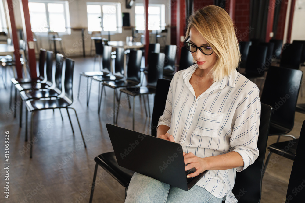 Photo of focused blonde woman working on laptop while sitting Photo of focused blonde woman working on laptop while sitting
