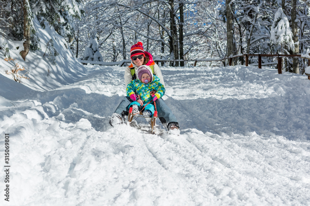 Mother and daughter speeding downhill on wooden sledge. Mother and daughter speeding downhill on wooden sledge.