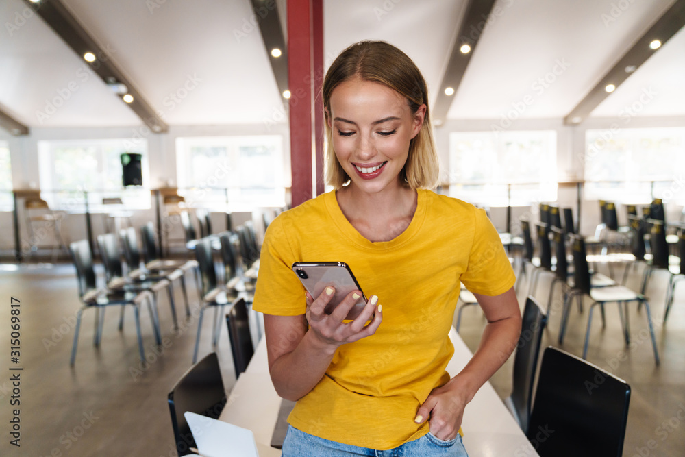 Photo of joyful blonde woman using cellphone and smiling while leaning
