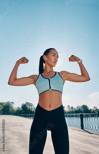 Fototapeta Naklejka Na Ścianę i Meble -  Strong and confident beautiful woman flexing her muscles
