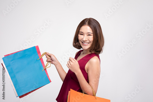 Shopping Asian woman with short hairs smile wearing red dress Holding Shopping bags,Cheerful and happiness emotional,Enjoy Shopping in black friday sale,Isolated on gray background,Shopping Concept