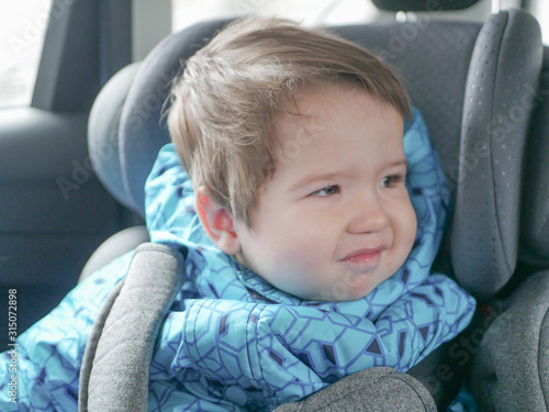 The child does not like to ride in a car seat. Dissatisfied child in a car seat. Preschool cute boy 1-2 years old, sitting in a safe car seat and crying during a family trip by car, bad mood, negative