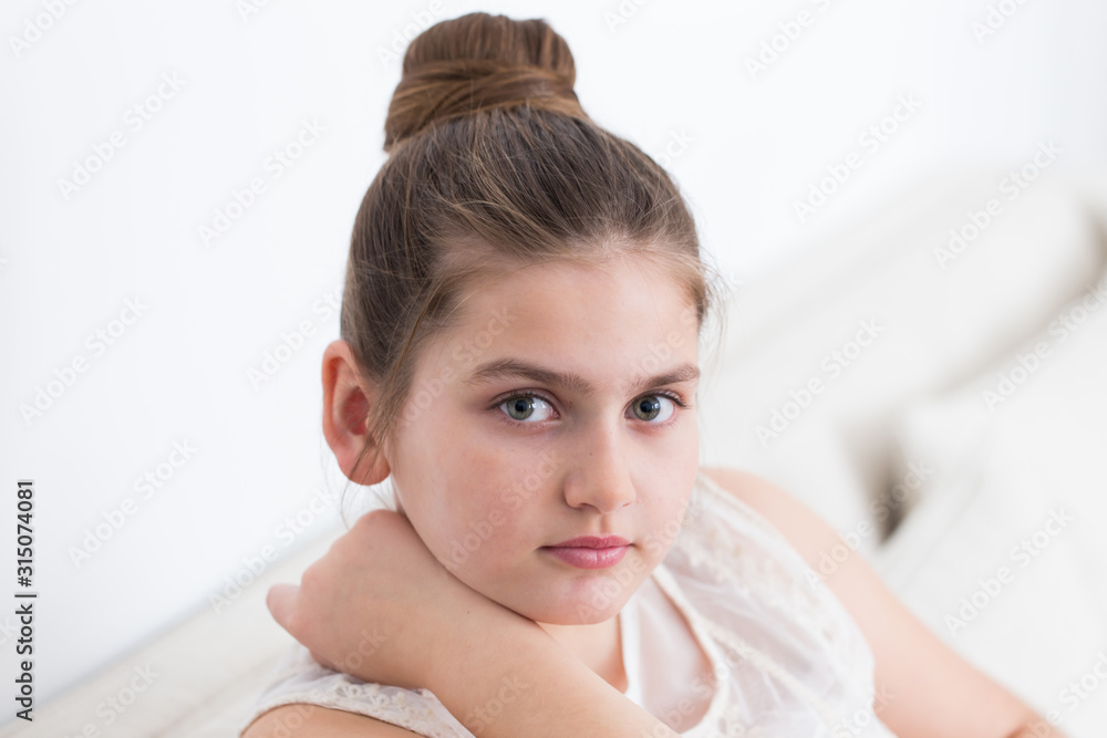 Closeup of pretty smiling young girl with dirty blond hair up in a bun dressed in lacy cream sleeveless top sitting in pale linen couch looking up Closeup of pretty smiling young girl with dirty blond hair up in a bun dressed in lacy cream sleeveless top sitting in pale linen couch looking up