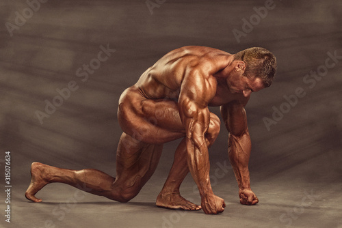 Handsome, Muscular, Naked Bodybuilder Kneeling on the Floor, Flexing Muscles