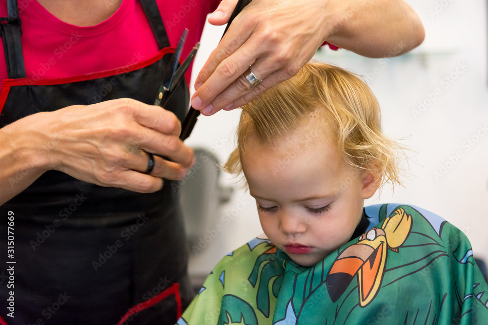 Fototapeta premium Cute blonde girl having her first haircut.