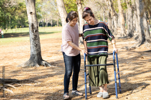Asian senior woman use walking aid during rehabilitation after knee surgery, young carer assisting reassuring mature elderly people practice walking with walker,female caregiver help,care,support