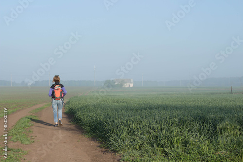 Woman traveler with backpack runs beautifyl atmospheric misty morning a house among fields in the background