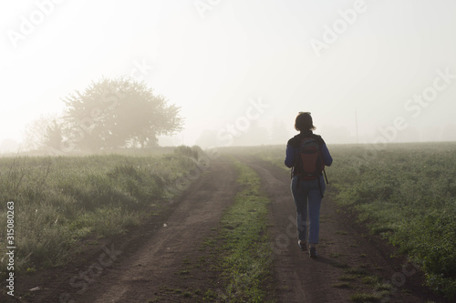 Back view of a woman traveler who walks in nature very beautiful atmospheric misty morning © Victoriia