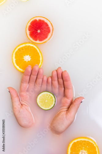 Lime in hands. Slice of yellow oranges and red grapefruit citrus fruits in murky muddy milky water.