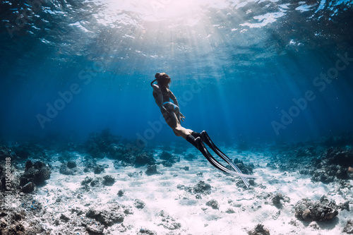 Woman free diver with fins glides underwater in deep blue ocean
