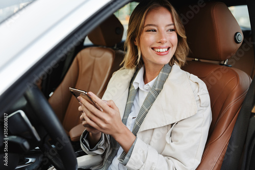 Image of beautiful businesslike woman sitting in car and using cellphone photo