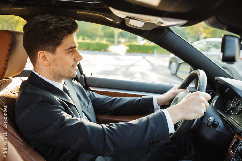 Image of young caucasian businesslike man in black suit driving car Image of young caucasian businesslike man in black suit driving car