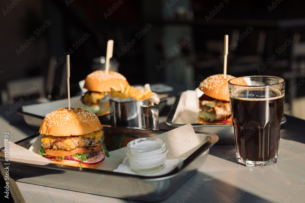 Tasty Burgers with French fries, cream sauce and dark beer on table.