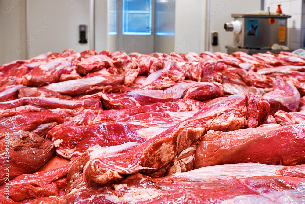 Fresh raw beef meat on the table and meat mincing machine in the background in a slaughterhouse