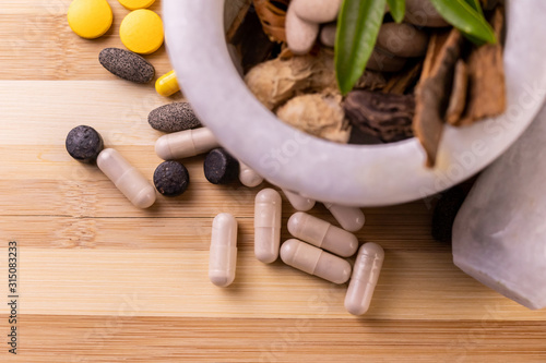 Top view macro shot of herbal pills and tablets arranged with spices on a red stone. Unani medicines concept.