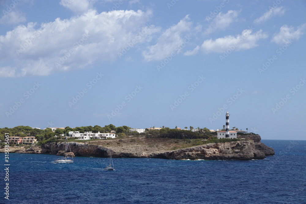 rocky coastline with a lighthouse, residential houses and two boats