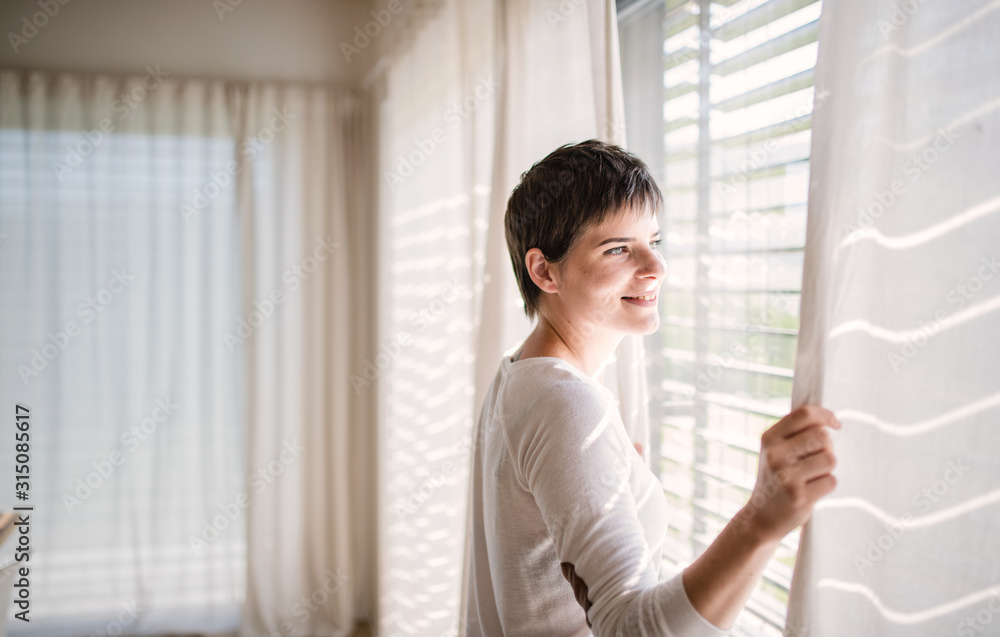 Portrait of young woman standing by window indoors at home. Portrait of young woman standing by window indoors at home.