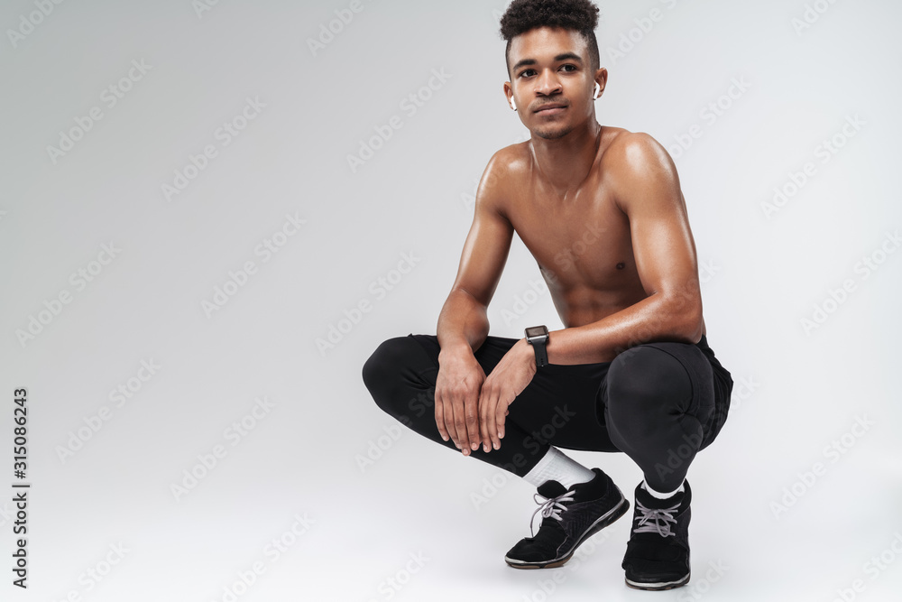 Photo of shirtless african american man using earpods while squatting Photo of shirtless african american man using earpods while squatting