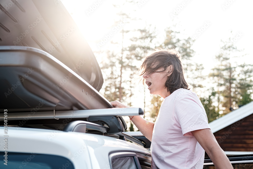 Woman looks into open trunk or cargo box, which is located on roof of the car and realizes that she forgot something important.
