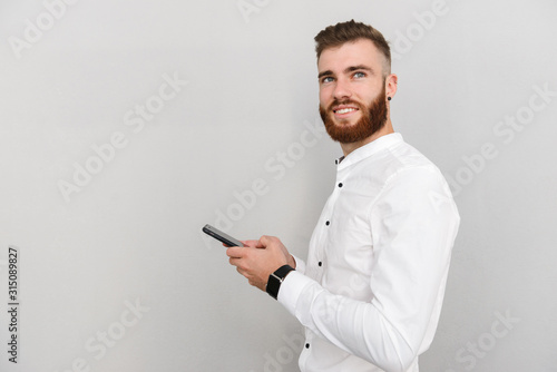 Image of bearded happy man smiling and typing on cellphone