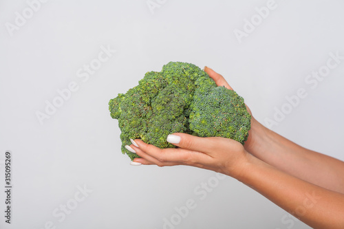 Closeup of female hands holding big green broccoli, fresh raw vegetables, concept of healthy eating and vegetarian diet, low calorie food nutrition. indoor studio shot, grey background, copy space