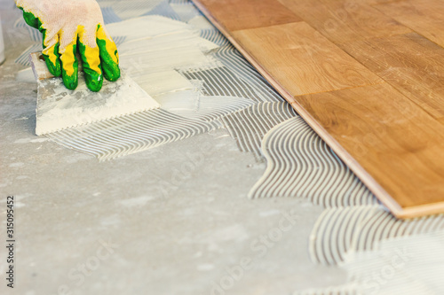 The master smears the glue on the concrete floor and lays the parquet, professional parquet laying.