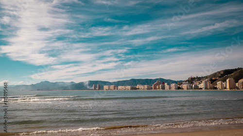 Sandy long beach with waves rolling on it on a sunny day by the Mediterranean sea in Valencia  Spain. A shot of tranquil and relaxing vacations in Spain.