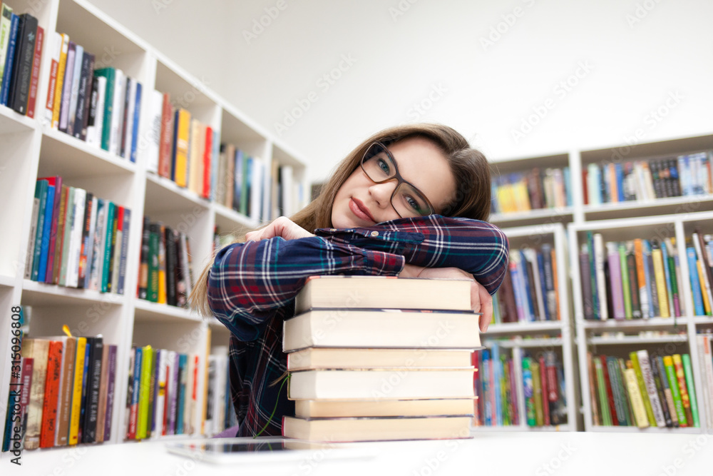 Beautiful student leaned her head on a pile of books. Young woman in library concept Beautiful student leaned her head on a pile of books. Young woman in library concept