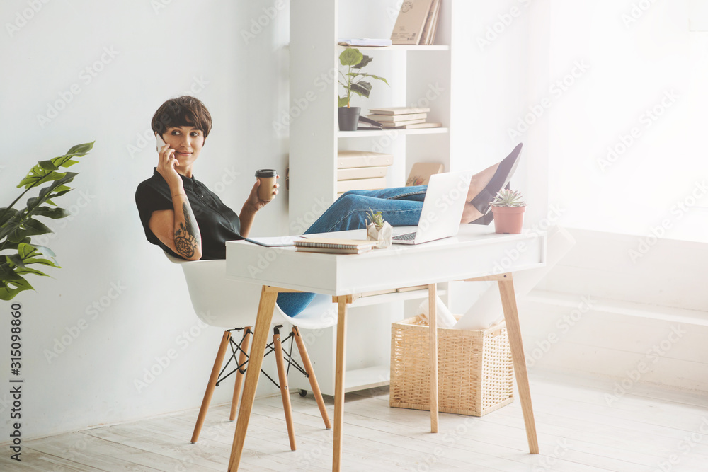 Pretty young businesswoman sitting in a chair with the legs over the desk and talking on phone. Pretty young businesswoman sitting in a chair with the legs over the desk and talking on phone.