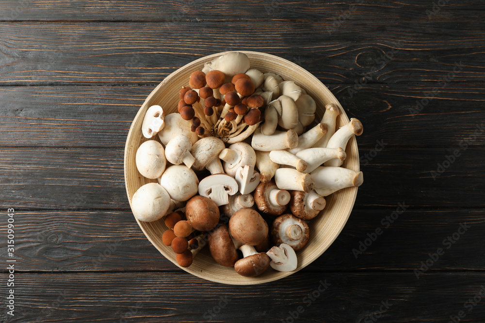 Different mushrooms in bowl on wooden background, top view Different mushrooms in bowl on wooden background, top view