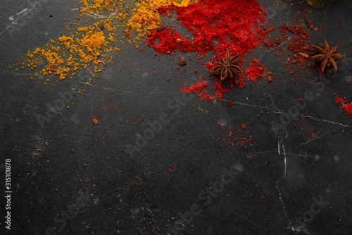 Different types of spices on a dark stone background, view from the top