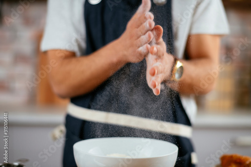 Young handsome chef in modern kitchen. Close up of man cleaning his hands of flour. 