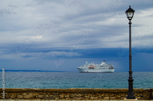 Classic small cruiseship or cruise ship liner Ocean Majesty of Majestic Cruises with street lantern in foreground on blue sea with blue sky and low clouds photo