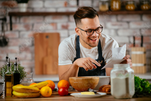 Portrait of handsome man in kitchen. Young man cooking while reading recipe. 