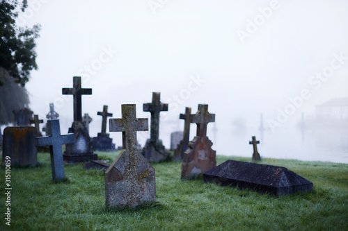 Crosses on gravestones in ethereal foggy cemetery photo