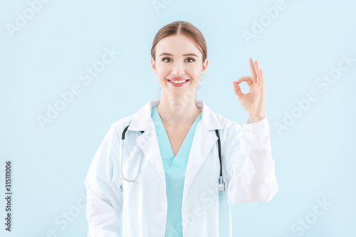 Portrait of female doctor showing OK gesture on light background
