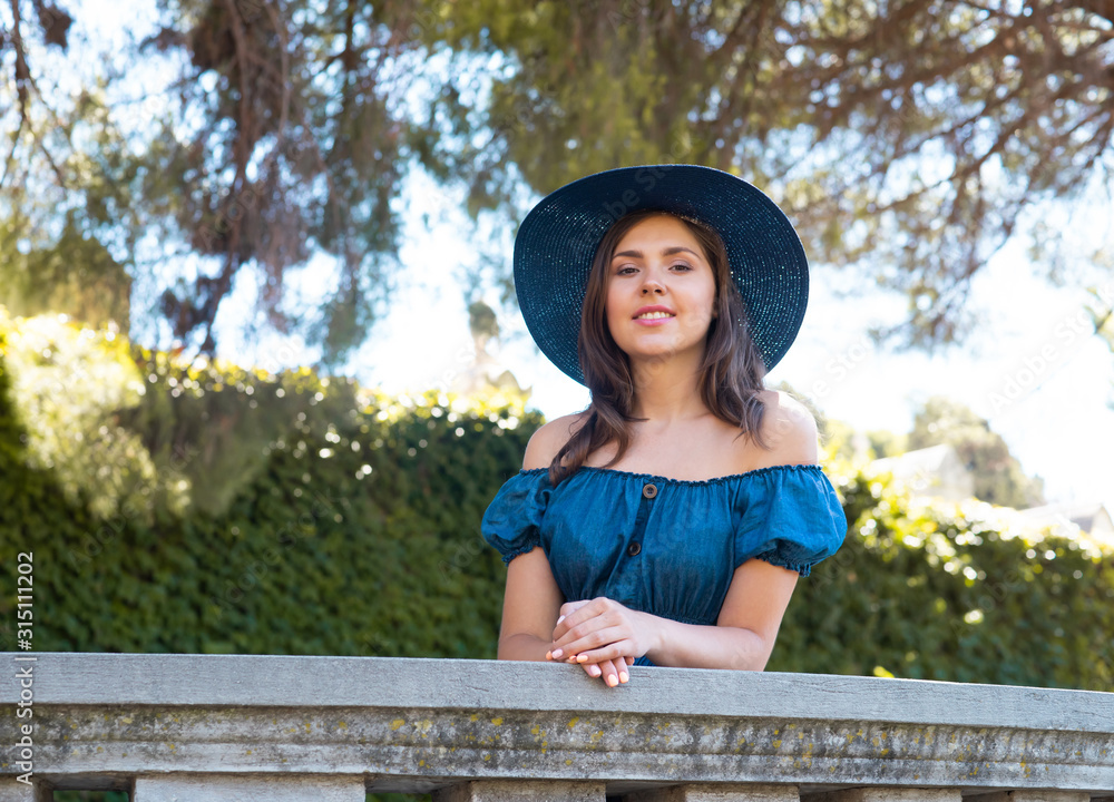 Young and beautiful brunette girl in dress and hat walking outdoor in the park. Nice, France. Summer vacation, traveling and tourism.
