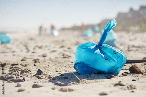 Blue bag of litter on sunny, sandy beach photo