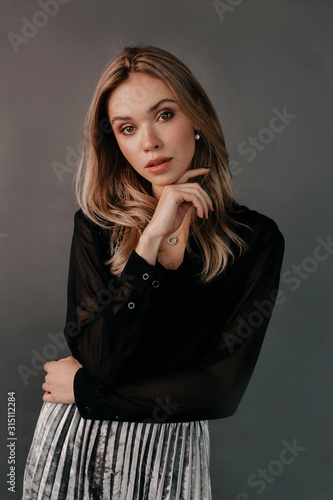 Elegant incredible blond woman posing at camera during photoshoot over grey background. Beauty girl with short hair and make-up.elegant lady in black dress