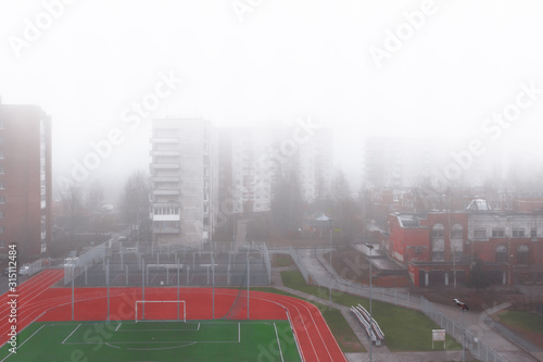 Fog over the city.Houses and a football field in the fog