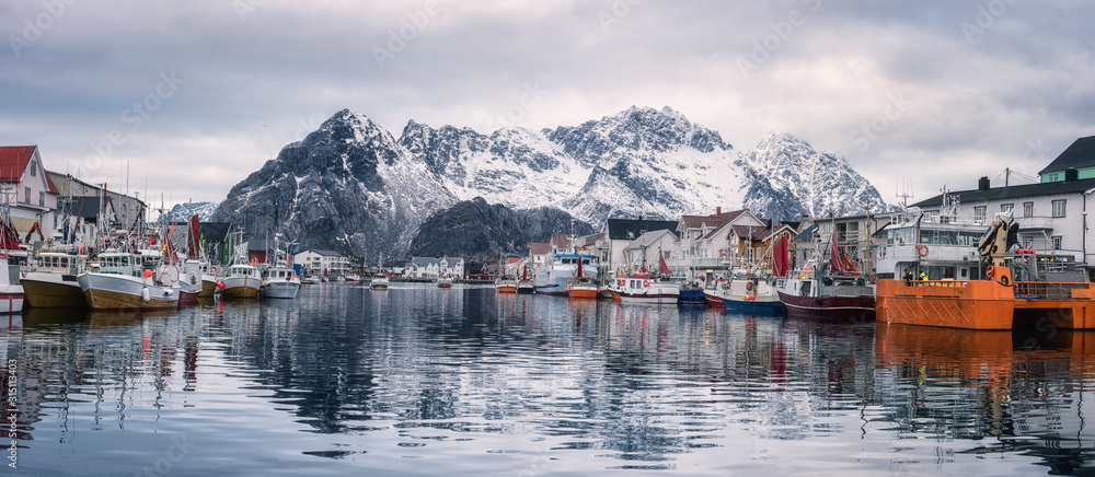 Panoramic view of Henningsvaer, cozy fishing village in Lofoten Islands, Northern Norway. Scenic landscape with mountains, houses, boats, sky and reflection in the water, outdoor travel background